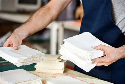 A person in a blue apron holding a stack of white paper towels