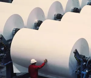 Industrial interior with large rolls of brown paper stacked on pallets.